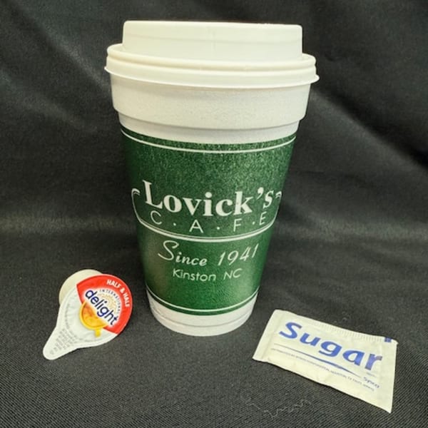 A Lovick's Cafe coffee cup, creamer, and sugar packet on a dark surface.