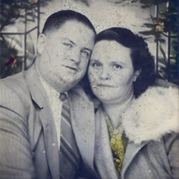 A vintage black and white photo of a man and woman posing closely together, with a hint of color.
