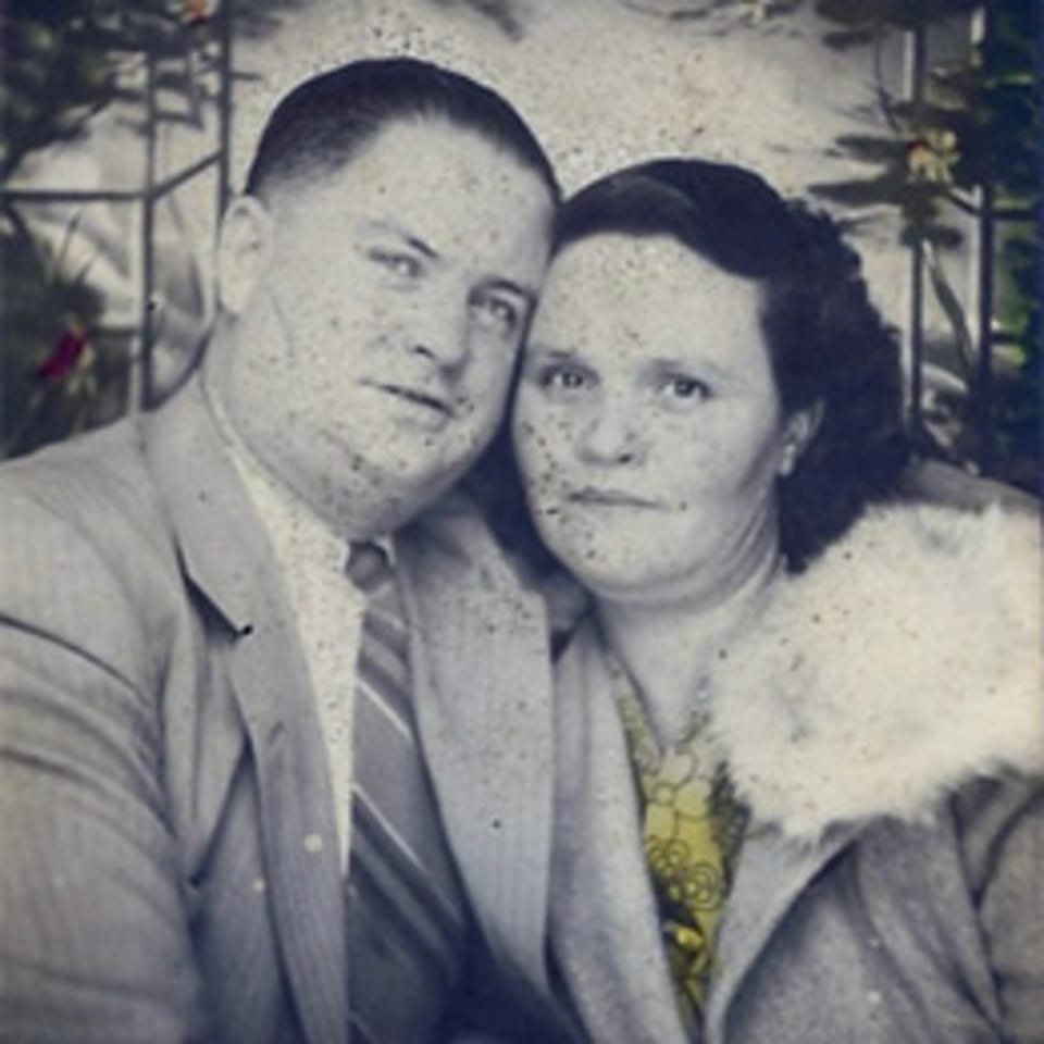 A vintage black and white photo of a man and woman posing closely together, with a hint of color.