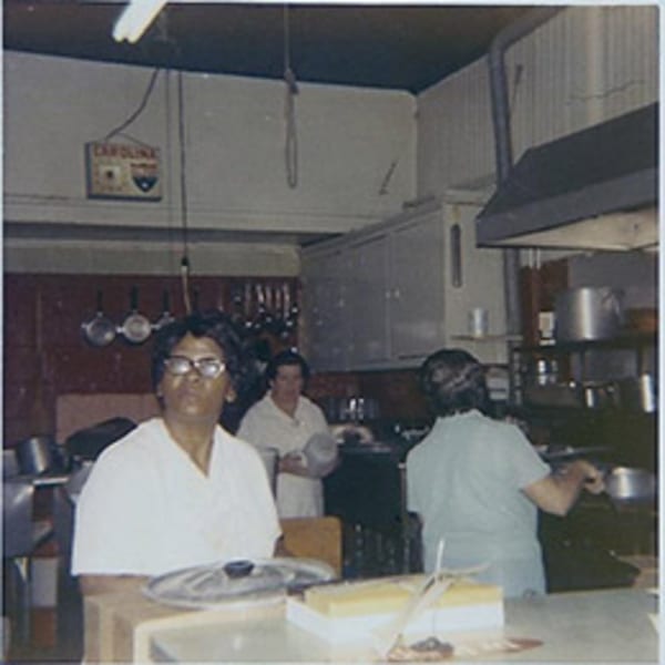 Three women working in a busy, vintage diner kitchen with pots and pans hanging.