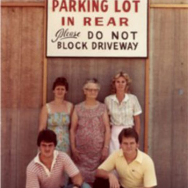 Five people, three women and two men, pose in front of a "PARKING LOT IN REAR" sign.