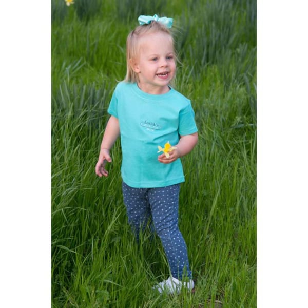 A smiling child in a Lovick's Cafe t-shirt holds a yellow flower in a grassy field.