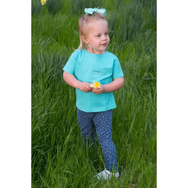 A young child wearing a Lovick's Cafe t-shirt and holding a yellow flower in a grassy field.