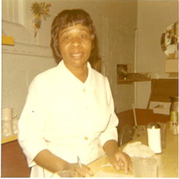 A smiling woman in a white uniform stands behind a counter, writing on paper at Lovick's Cafe.