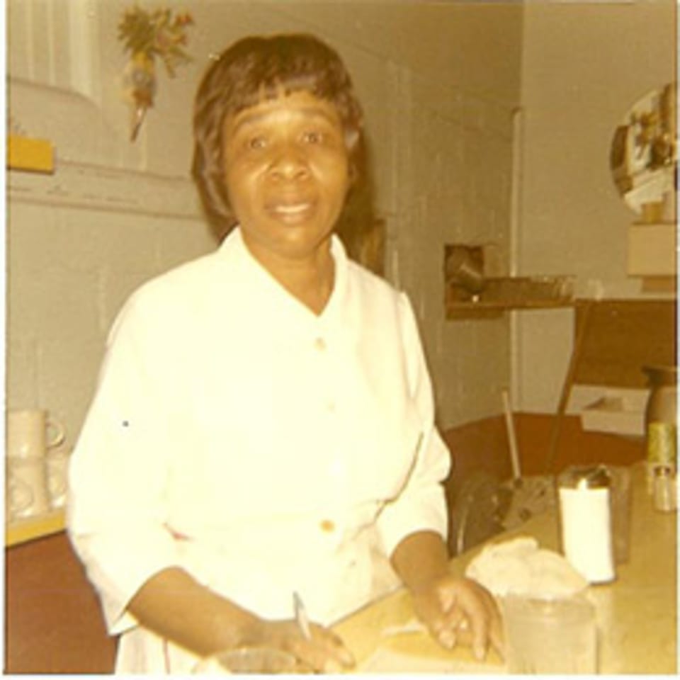 A smiling woman in a white uniform stands behind a counter, writing on paper at Lovick's Cafe.