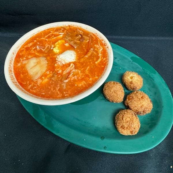 A white bowl of red soup with white and yellow chunks, served with four fried hushpuppies on a green plate.