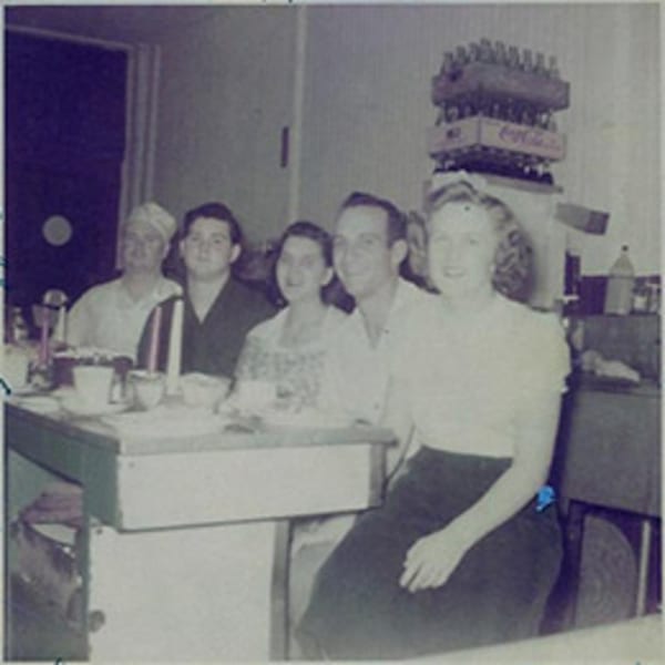 Five people, including a chef, gathered around a table with drinks and a Coca-Cola crate.