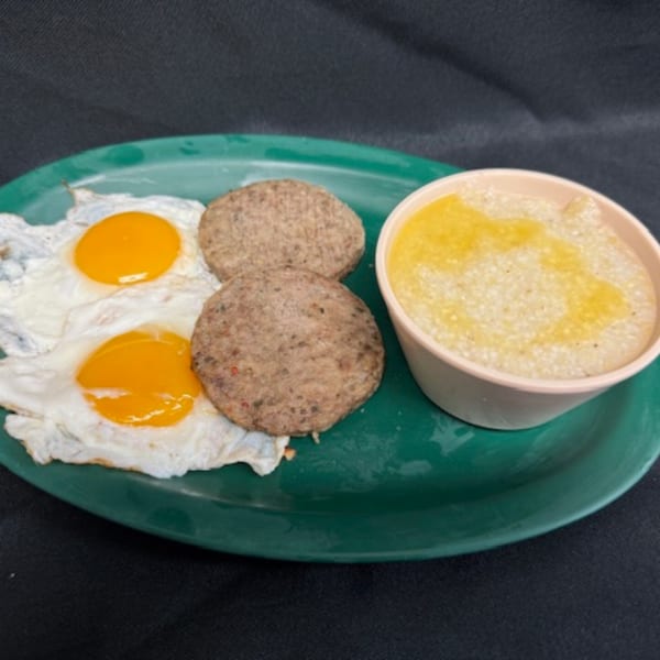 A diner breakfast on a green plate with two fried eggs, two sausage patties, and a cup of grits.